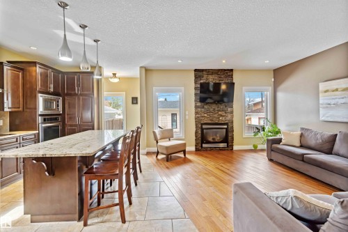 Open-concept living space with a stone-clad fireplace, hardwood flooring, and recessed lighting - 10630 82 Street, Edmonton, AB - Indoor With Fireplace