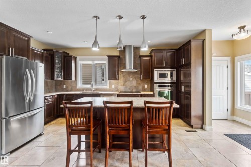 Spacious kitchen featuring dark wood cabinetry, stainless steel appliances, a center island, pendant lighting, and tiled flooring - 10630 82 Street, Edmonton, AB - Indoor Photo Showing Other Room