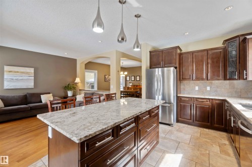 Open-concept kitchen featuring a large island with a stone countertop, dark wood cabinetry, and stainless steel appliances - 10630 82 Street, Edmonton, AB - Indoor Photo Showing Kitchen With Upgraded Kitchen