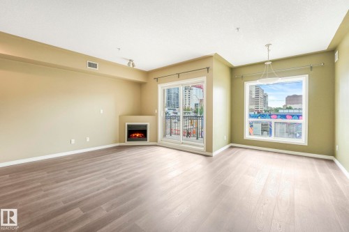Unfurnished living room featuring a warm lit fireplace and light wood-style floors - 310 10606 102 Avenue, Edmonton, AB - Indoor With Fireplace