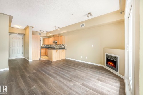 Unfurnished living room featuring a lit fireplace, track lighting, dark wood finished floors, and a textured ceiling - 310 10606 102 Avenue, Edmonton, AB - Indoor With Fireplace