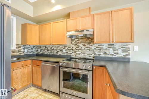 Kitchen with stainless steel appliances, dark countertops, tasteful backsplash, under cabinet range hood, and light brown cabinetry - 310 10606 102 Avenue, Edmonton, AB - Indoor Photo Showing Kitchen