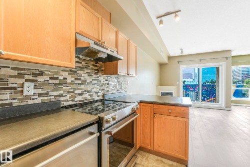 Kitchen with dark countertops, stainless steel appliances, a peninsula, decorative backsplash, and under cabinet range hood - 310 10606 102 Avenue, Edmonton, AB - Indoor Photo Showing Kitchen
