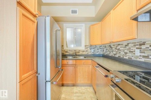 Kitchen with tasteful backsplash, appliances with stainless steel finishes, under cabinet range hood, light brown cabinetry, and dark countertops - 310 10606 102 Avenue, Edmonton, AB - Indoor Photo Showing Kitchen With Double Sink