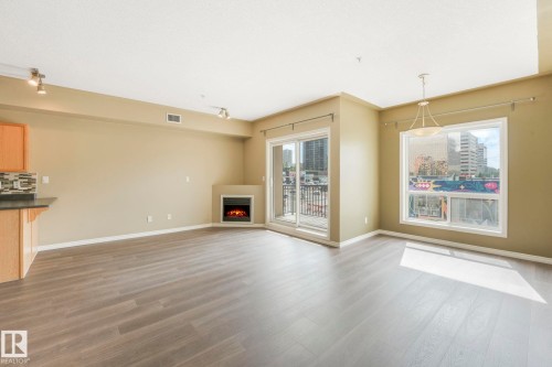 Unfurnished living room featuring wood finished floors and a warm lit fireplace - 310 10606 102 Avenue, Edmonton, AB - Indoor Photo Showing Other Room With Fireplace