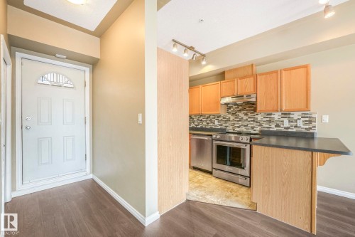 Kitchen with appliances with stainless steel finishes, dark countertops, a breakfast bar area, and dark wood-style flooring - 310 10606 102 Avenue, Edmonton, AB - Indoor Photo Showing Other Room