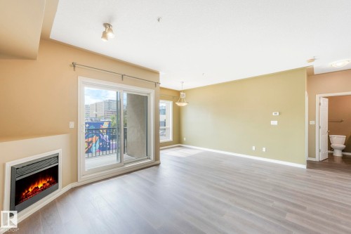 Unfurnished living room featuring wood finished floors and a warm lit fireplace - 310 10606 102 Avenue, Edmonton, AB - Indoor With Fireplace
