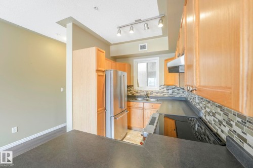 Kitchen with tasteful backsplash, dark countertops, high end refrigerator, under cabinet range hood, and range with electric cooktop - 310 10606 102 Avenue, Edmonton, AB - Indoor Photo Showing Kitchen