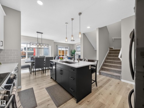 Modern kitchen featuring a central island with white countertop, integrated sink, and pendant lighting - 323 Balsam Link, Leduc, AB - Indoor Photo Showing Kitchen With Upgraded Kitchen