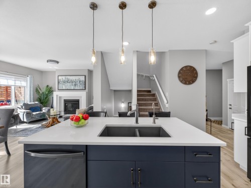 Kitchen island featuring a dual basin sink, white countertop, and dark blue cabinetry with brass hardware - 323 Balsam Link, Leduc, AB - Indoor Photo Showing Kitchen With Fireplace With Double Sink With Upgraded Kitchen