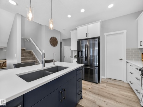 Contemporary kitchen island featuring a dual-basin undermount sink, a chrome faucet, and dark blue cabinetry with matte black hardware - 323 Balsam Link, Leduc, AB - Indoor Photo Showing Kitchen With Double Sink With Upgraded Kitchen