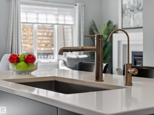 Kitchen island featuring a dual-handle faucet and a water filtration faucet in a bronze finish, integrated sink, and light-toned solid surface countertop - 323 Balsam Link, Leduc, AB - Indoor Photo Showing Kitchen