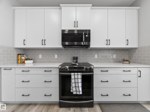 Kitchen featuring crisp white cabinetry with matte black hardware, light-toned subway tile backsplash, solid surface countertops, and a black stainless steel range with matching microwave - 323 Balsam Link, Leduc, AB - Indoor Photo Showing Kitchen