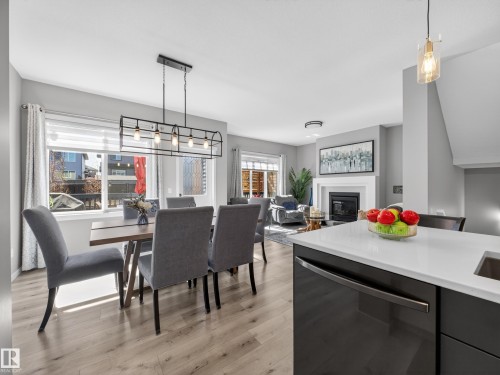 Open-concept dining area featuring wood-finish flooring, a contemporary linear chandelier, and ample natural light from large windows - 323 Balsam Link, Leduc, AB - Indoor Photo Showing Dining Room With Fireplace