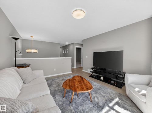 Open-concept living space featuring wood-finish flooring, a contemporary ceiling light fixture, and a partial wall with a white cap - 323 Balsam Link, Leduc, AB - Indoor Photo Showing Living Room