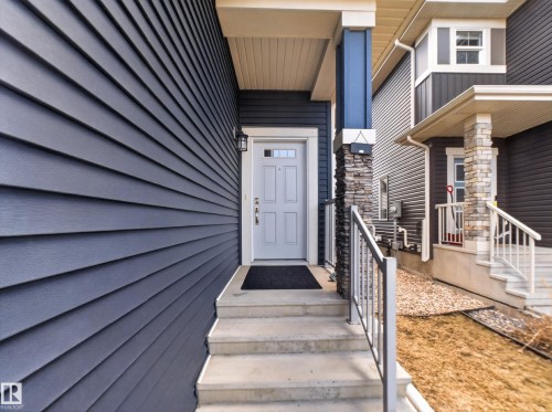 Entryway featuring a light gray door with decorative glass, concrete steps, and a metal handrail - 323 Balsam Link, Leduc, AB - Outdoor With Deck Patio Veranda