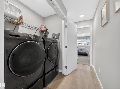 Dedicated laundry area featuring modern front-load appliances, wire shelving, and wood-finish flooring - 323 Balsam Link, Leduc, AB - Indoor Photo Showing Laundry Room