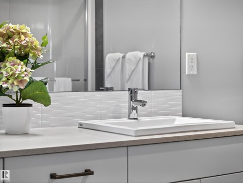 Modern vanity featuring a rectangular undermount sink, chrome faucet, textured white tile backsplash, and light-toned countertop - 323 Balsam Link, Leduc, AB - Indoor Photo Showing Bathroom
