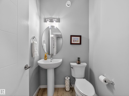 Contemporary powder room featuring a pedestal sink with chrome faucet, an oval wall mirror, and vanity lighting - 323 Balsam Link, Leduc, AB - Indoor Photo Showing Bathroom