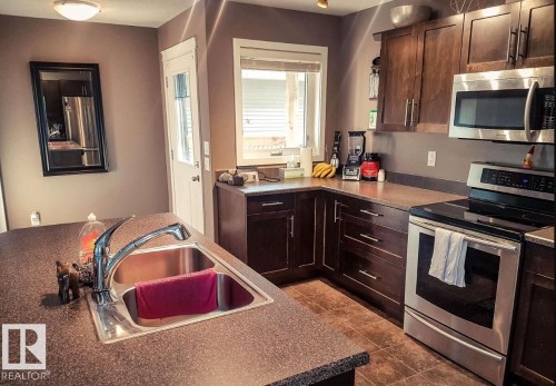 Kitchen with stainless steel appliances, dark brown cabinets, dark tile patterned floors, and dark countertops - 12246 103 Street Nw, Edmonton, AB - Indoor Photo Showing Kitchen With Double Sink