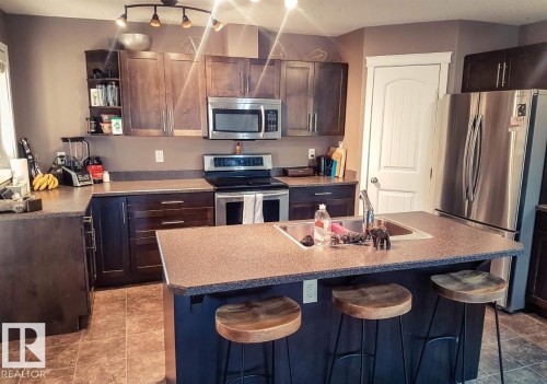 Kitchen with appliances with stainless steel finishes, a kitchen breakfast bar, dark brown cabinets, a center island with sink, and open shelves - 12246 103 Street Nw, Edmonton, AB - Indoor Photo Showing Kitchen With Double Sink