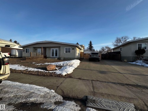 The property features a light-colored exterior, a front porch with decorative lattice, and a paved driveway leading to the rear of the home - 11452 152B Avenue, Edmonton, AB - Outdoor