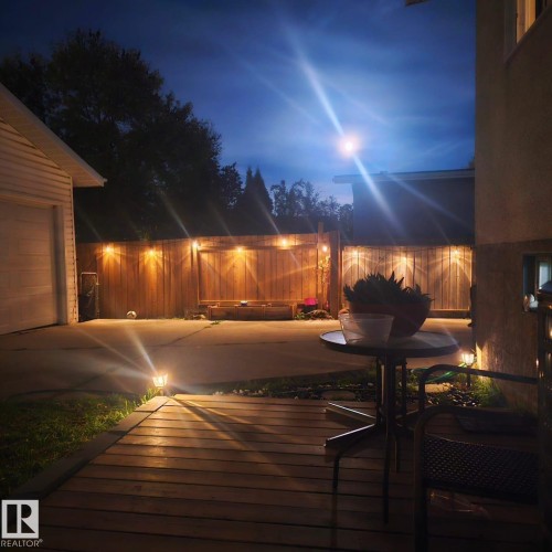 The property features a wooden deck area with a view of the backyard, complete with a wooden fence and ambient lighting - 11452 152B Avenue, Edmonton, AB - Outdoor