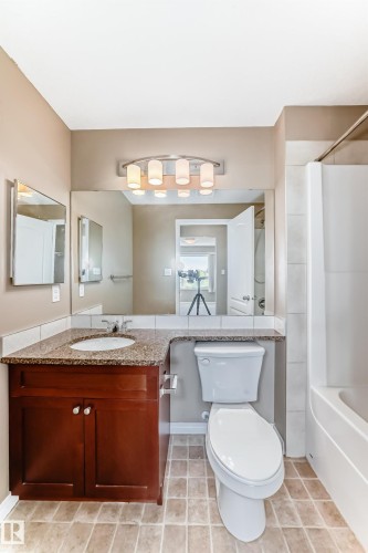 Bathroom featuring a wood-finish vanity with a granite-style countertop, undermount sink, and a large wall-mounted mirror - 344 1520 Hammond Gate Gate, Edmonton, AB - Indoor Photo Showing Bathroom