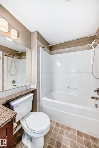 Bathroom featuring a white bathtub and shower combination, a white toilet, and a vanity with a granite-style countertop - 344 1520 Hammond Gate Gate, Edmonton, AB - Indoor Photo Showing Bathroom