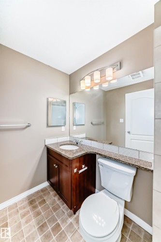 Bathroom featuring a wood-finish vanity with an integrated sink, a granite countertop, and a full-width mirror - 344 1520 Hammond Gate Gate, Edmonton, AB - Indoor Photo Showing Bathroom