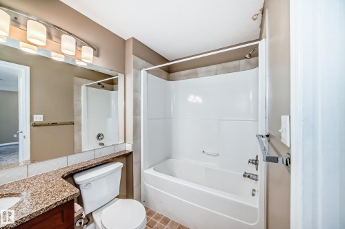 Bathroom featuring a white bathtub/shower combination with tile surround, a vanity with a granite-look countertop, integrated sink, and a large mirror - 344 1520 Hammond Gate Gate, Edmonton, AB - Indoor Photo Showing Bathroom