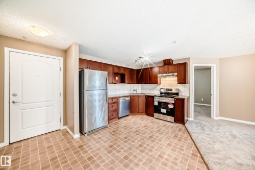 Kitchen featuring stainless steel appliances, dark wood cabinetry, and a white tile backsplash - 344 1520 Hammond Gate Gate, Edmonton, AB - Indoor Photo Showing Kitchen
