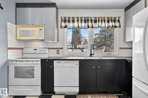 Kitchen featuring black lower cabinetry, white subway tile backsplash with a red accent band, and an undermount sink with a gooseneck faucet - 9112 130 Avenue, Edmonton, AB - Indoor Photo Showing Kitchen