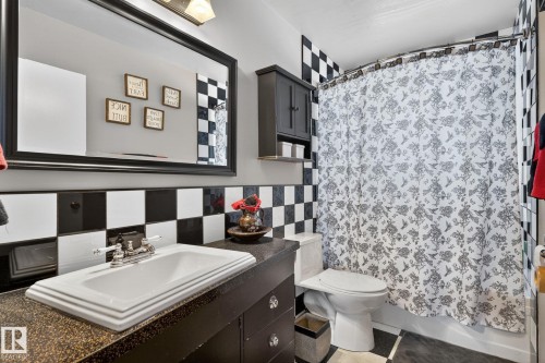 Bathroom featuring a rectangular sink, dark vanity with cabinet storage, black and white checkered wall tiling, and a patterned shower curtain - 9112 130 Avenue, Edmonton, AB - Indoor Photo Showing Bathroom