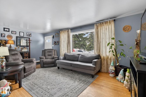 Bright living area featuring wood-finish flooring, a large picture window, and a white paneled entrance door - 9112 130 Avenue, Edmonton, AB - Indoor Photo Showing Living Room