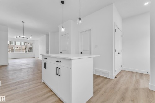Kitchen island featuring white cabinetry with matte black hardware, a light-toned countertop, and two pendant light fixtures - 277 Munn Way, Leduc, AB - Indoor