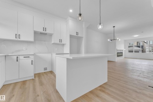 White kitchen featuring flat-panel cabinetry with matte black hardware, stone-finish countertops, and a full-height backsplash - 277 Munn Way, Leduc, AB - Indoor Photo Showing Kitchen