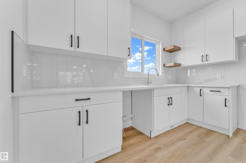 Contemporary kitchen featuring white cabinetry with matte black hardware, light-toned wood-finish flooring, a stainless steel sink, and a white countertop with a matching backsplash - 277 Munn Way, Leduc, AB - Indoor Photo Showing Kitchen