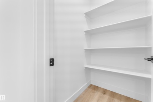 White shelving system with four tiers of storage, light wood-finish flooring, and a white door with dark hardware - 277 Munn Way, Leduc, AB - Indoor With Storage