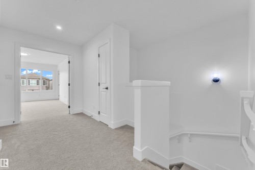 Light gray carpeted hallway featuring white walls and trim, with a modern wall sconce and recessed lighting - 277 Munn Way, Leduc, AB - Indoor Photo Showing Other Room