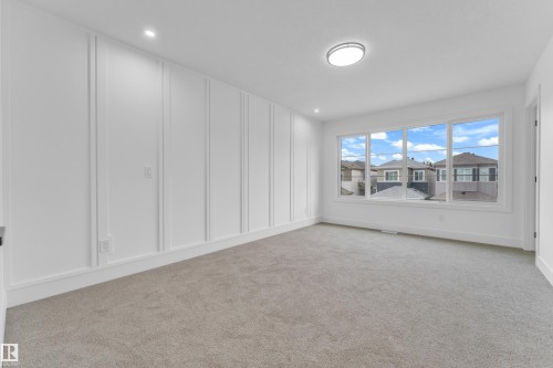 Bright interior room with extensive white wall paneling, light gray carpeting, recessed ceiling lighting, and a prominent window array offering multiple panes - 277 Munn Way, Leduc, AB - Indoor Photo Showing Other Room
