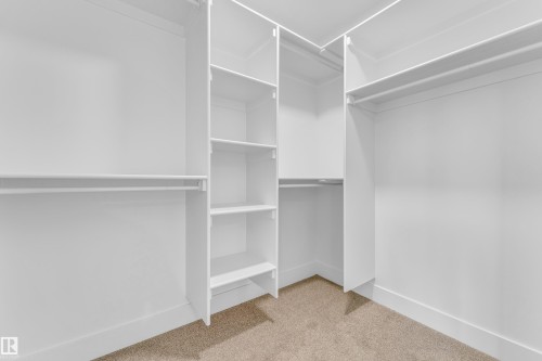 Custom built-in closet system featuring multiple hanging rods, integrated shelving units, and neutral carpeting - 277 Munn Way, Leduc, AB - Indoor With Storage