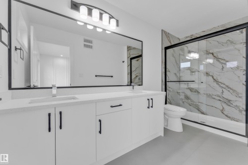 Contemporary bathroom featuring a dual vanity with white cabinetry, quartz-finish countertops, and black hardware - 277 Munn Way, Leduc, AB - Indoor Photo Showing Bathroom