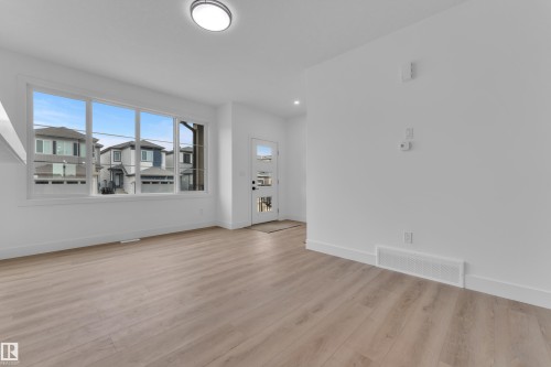 Spacious room featuring light wood-finish flooring, white baseboards, and a large multi-pane window - 277 Munn Way, Leduc, AB - Indoor