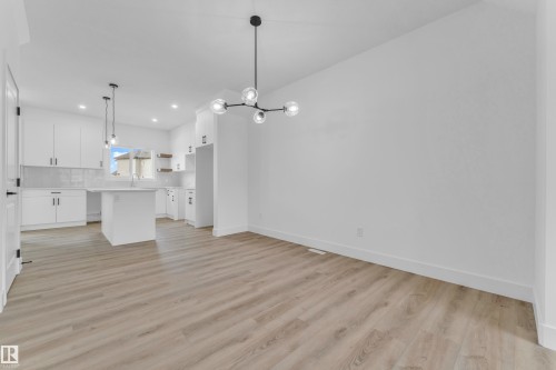 Open-concept living space featuring wood-finish flooring, a modern chandelier, and a kitchen with white cabinetry, a center island, and subway tile backsplash - 277 Munn Way, Leduc, AB - Indoor Photo Showing Kitchen