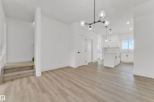 Expansive open-concept living area featuring light wood-finish flooring, a modern linear chandelier, and crisp white walls - 277 Munn Way, Leduc, AB - Indoor Photo Showing Kitchen
