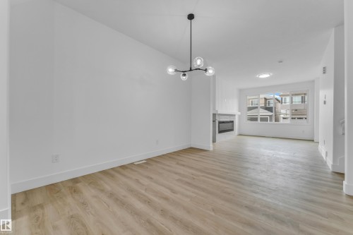 Bright open-concept interior featuring light wood-finish flooring, a modern linear fireplace with a white mantel, and a contemporary spherical chandelier - 277 Munn Way, Leduc, AB - Indoor