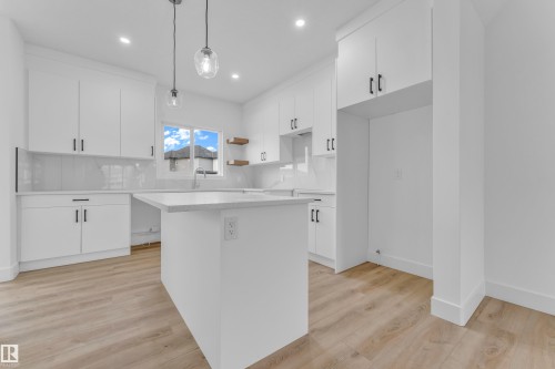 Modern kitchen featuring a central island, white cabinetry with black hardware, light-toned wood-finish flooring, and pendant lighting - 277 Munn Way, Leduc, AB - Indoor Photo Showing Kitchen