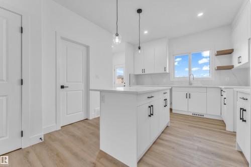Modern kitchen featuring a central island with pendant lighting, white cabinetry with matte black hardware, light-toned wood-finish flooring, and a window with a stainless steel faucet - 277 Munn Way, Leduc, AB - Indoor Photo Showing Kitchen