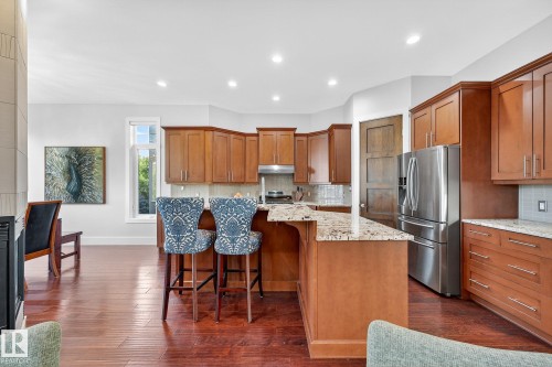 Kitchen featuring brown cabinetry, a kitchen bar, appliances with stainless steel finishes, light stone countertops, and an island with sink - 940 Haliburton Road, Edmonton, AB - Indoor Photo Showing Kitchen